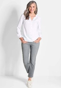 Weiße Langarmbluse mit geknöpftem V-Ausschnitt, kombiniert mit hellgrauen Slim-Fit-Jeans und weißen Sneakers. Einfaches, sauberes Design.