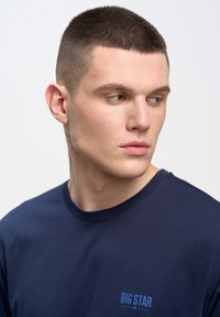 Navy krāsas T-krekls, izgatavots no kokvilnas, ar apaļu kakla izgriezumu un mazu zilu "BIG STAR" logotipu uz krūškurvja. Gluda tekstūra.