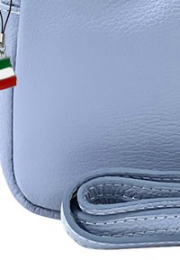 Lichtblauwe leren schoudertas met een gestructureerd oppervlak, voorzien van een hangende hanger van de Italiaanse vlag en een gerolde schouderband.