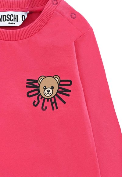 Sweatshirt rose avec un col rond, détails de boutons sur une épaule, présentant un graphique d'ours et le texte "MOSCHINO" en noir.