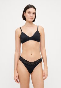 Crni bralet s tankim podesivim trakama i glatkom teksturom, u kombinaciji s crnim tangama s čipkastim obrubom i valovitim rubovima.