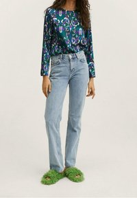 Maglietta a maniche lunghe con un motivo floreale verde, viola e bianco; jeans a vita alta di colore blu chiaro; pantofole verdi e morbide con aperture per le dita.