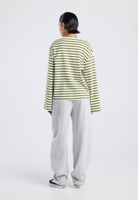 Camisa de manga larga a rayas verdes y blancas combinada con pantalones de chándal grises sueltos, que presentan un corte relajado y una textura de algodón suave.