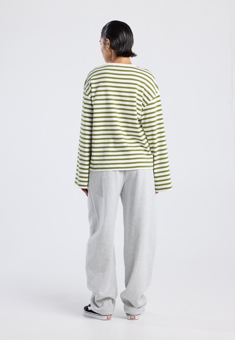 Camisa de manga larga a rayas verdes y blancas combinada con pantalones de chándal grises sueltos, que presentan un corte relajado y una textura de algodón suave.