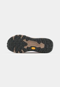 La semelle extérieure Vibram présente une base en caoutchouc noir avec des rainures profondes et une semelle intermédiaire beige. Logo Vibram en jaune, intégré dans le design.