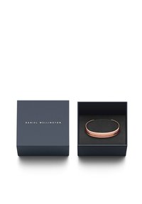 Atidaryta tamsiai mėlyna Daniel Wellington dėžutė su rožių aukso apyranke viduje, padėta ant juodos putos.