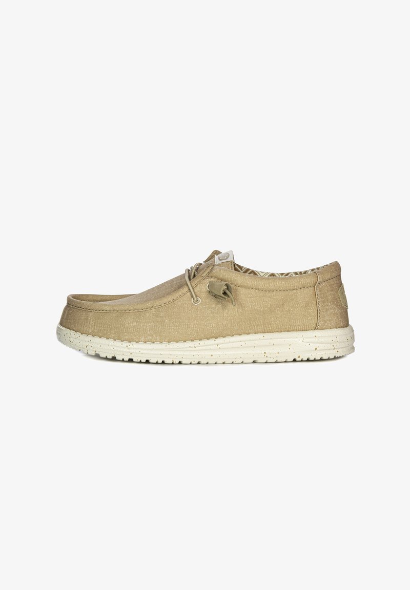 Beige canvas schoen met een ronde neus, beige veters en een gemêleerde witte rubberen zool. Het interieur heeft een geometrisch patroon.