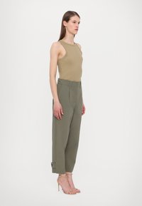 Tan tank top, loose olive green trousers with a cuff and button detail, and nude strappy high heels. Smooth textures throughout.