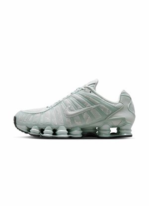 Lichtgroene Nike sportschoen met witte mesh bovenkant, zichtbare dempingsveren in de zool en een zilveren Nike swoosh-logo aan de zijkant.