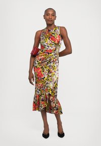 Multicolored floral dress with a fitted silhouette, side slit, and ruffled hem. Paired with a small red handbag and black pointed shoes.