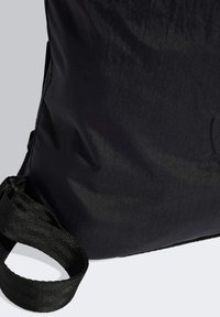 Sort nylon taske med en tekstureret overflade, en justerbar rem og en buet form. Minimalistisk design uden synlige logoer eller pynt.