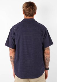 Chemise à manches courtes en bleu marine foncé avec un motif texturé. Elle dispose d'un col et d'une petite étiquette logo au dos, fabriquée en tissu léger.