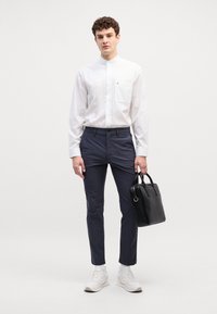 Camicia bianca con colletto, pantaloni slim-fit blu navy e sneakers bianche. Borsa in pelle nera con manici corti e inserti dorati.