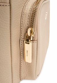 Beżowy, teksturowany narożnik torby ze skóry z złotym zamkiem błyskawicznym i prostokątnym, złotym uchwytem zamka błyskawicznego z wygrawerowanym napisem "COACH".