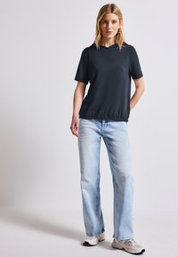 Top negro de manga corta con capucha y dobladillo elástico, combinado con jeans rectos de color azul claro y zapatillas color beige.