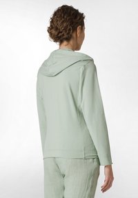 Sudadera verde claro de manga larga con un corte relajado, tejido suave y capucha con cordón; presenta costuras planas y un diseño sencillo.