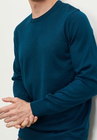 Miętowy sweter wykonany z miękkiego materiału, z okrągłym dekoltem i prążkowanymi mankietami. Czysty design bez widocznych wzorów ani elementów metalowych.