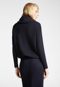 Top blu navy con un design testurizzato a righe e cappuccio. Vestibilità ampia con maniche lunghe e schiena drappeggiata, abbinato a un pantalone coordinato.