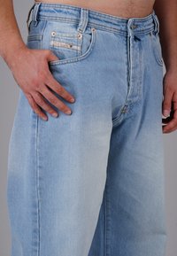 Hellblaue Jeans aus Denim mit geradem Schnitt, ausgestattet mit Kupferbeschlägen, Fronttaschen und dezenten Nahtdetails.