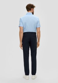 Himmelblaues Kurzarmhemd mit Kragen, kombiniert mit navyblauen Hosen. Die Hosen haben zwei Gesäßtaschen und werden mit weißen Sneakers getragen.