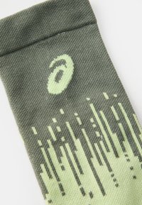 Calcetín verde y verde claro con un patrón, fabricado con un tejido texturizado y un logo. Presenta un diseño degradado con líneas verticales de distintos grosores.