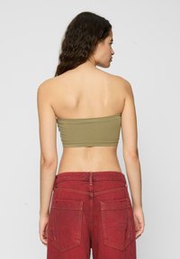 Olívovo zelený priliehavý bandeau top z elastického materiálu, skombinovaný s červenými nohavicami s vysokým pásom, ktoré majú zadné vrecká a kontrastné švy.