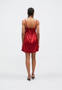 Rochie din satin roșu cu bretele subțiri, bust strâns la piept și fustă evazată. Textură netedă, până la genunchi, design simplu.