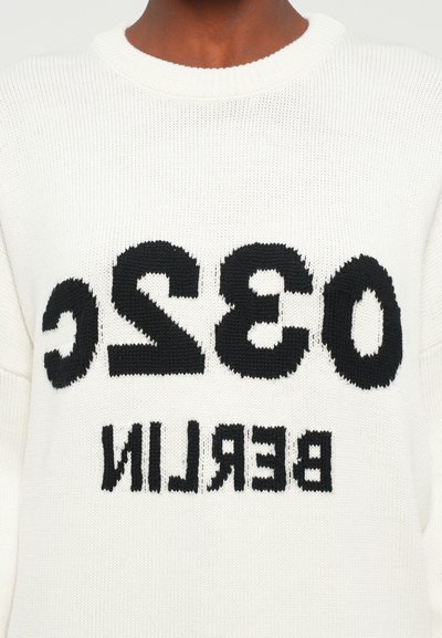 White knitted sweater featuring bold black lettering "032C BERLIN" across the front. The design has a ribbed crew neckline and textured pattern.