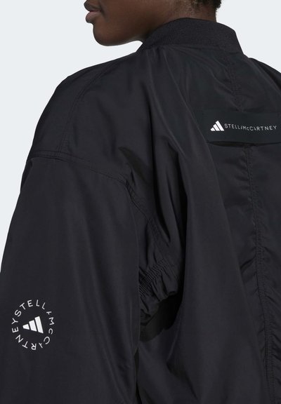 Fekete bomber dzseki bordázott gallérral és rugalmas mandzsettákkal. A hátsó részen egy feltűnő logófolt, a kézen pedig egy kör alakú logó található.