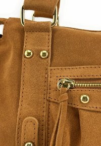 Détail d'un sac à main en daim marron présentant des accessoires en or, y compris une poche zippée, des coutures décoratives et une bandoulière avec des accents métalliques.