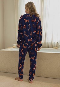 Navy pyjamapak met een speelse hondenprint in verschillende kleuren. Het bovenstuk heeft lange mouwen, terwijl de broek een elastische tailleband en boorden heeft.