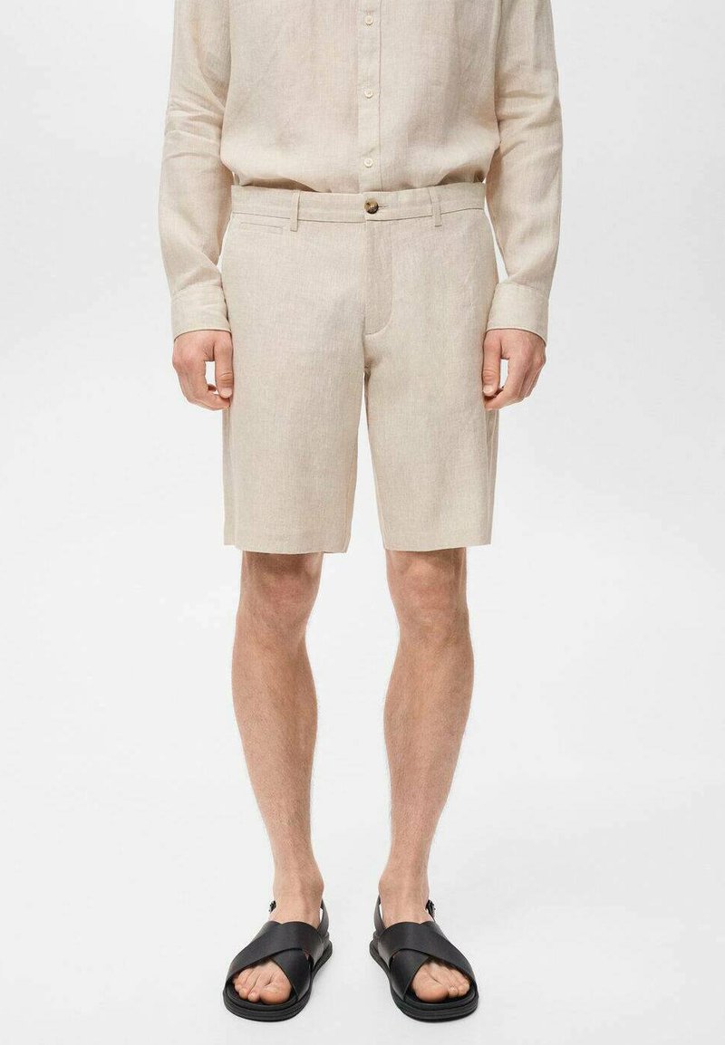 Beiga linnebyxor med skräddarsydd design, framfickor och en enda knappstängning. Bärs med svarta sandaler.