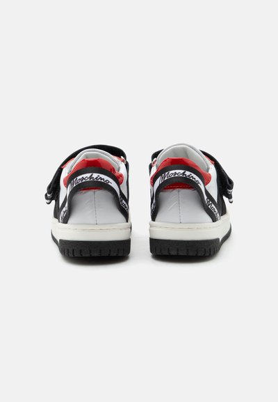 Ζεύγος λευκών, μαύρων και κόκκινων sneakers με μαύρες ρυθμιζόμενες λωρίδες με το λογότυπο "Moschino" στο πίσω μέρος, εμφανίζεται από πίσω σε απλό φόντο.