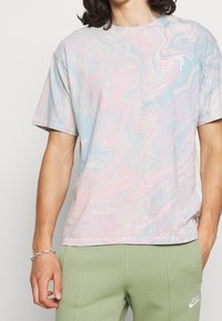 T-shirt à manches courtes avec un motif tourbillon pastel, principalement bleu et rose, fabriqué en tissu doux. Présente le logo Levis en blanc sur la poitrine.