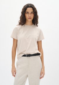 Beige katoenen t-shirt met een ronde hals, korte mouwen en een relaxte pasvorm, gecombineerd met lichtbeige hoge taillebroeken en een zwarte riem.