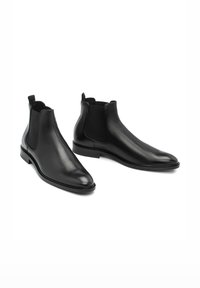 Botas Chelsea de cuero negro que presentan un diseño elegante, paneles laterales elásticos, una tira en la parte superior y un tacón bajo apilado para mayor simplicidad y comodidad al usarlas.