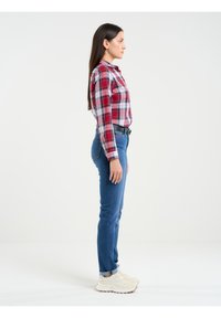 Sarkans, balts un zils checks krekls, apvienots ar piegulošām zilām džinsām. Kurpes ir gaiši beiges ar teksturētu dizainu. Sāniska profila skats.