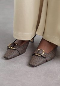 Chaussures à talons hauts brunes à motifs, avec des bouts pointus, présentant une boucle décorative et un talon bas. Design fermé en matériau texturé.