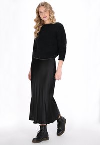 Zwarte donzige trui met driekwartmouwen, gecombineerd met een zwarte satijnen rok tot halverwege de benen. Draagt zwarte veterschoenen met een combat-stijl.