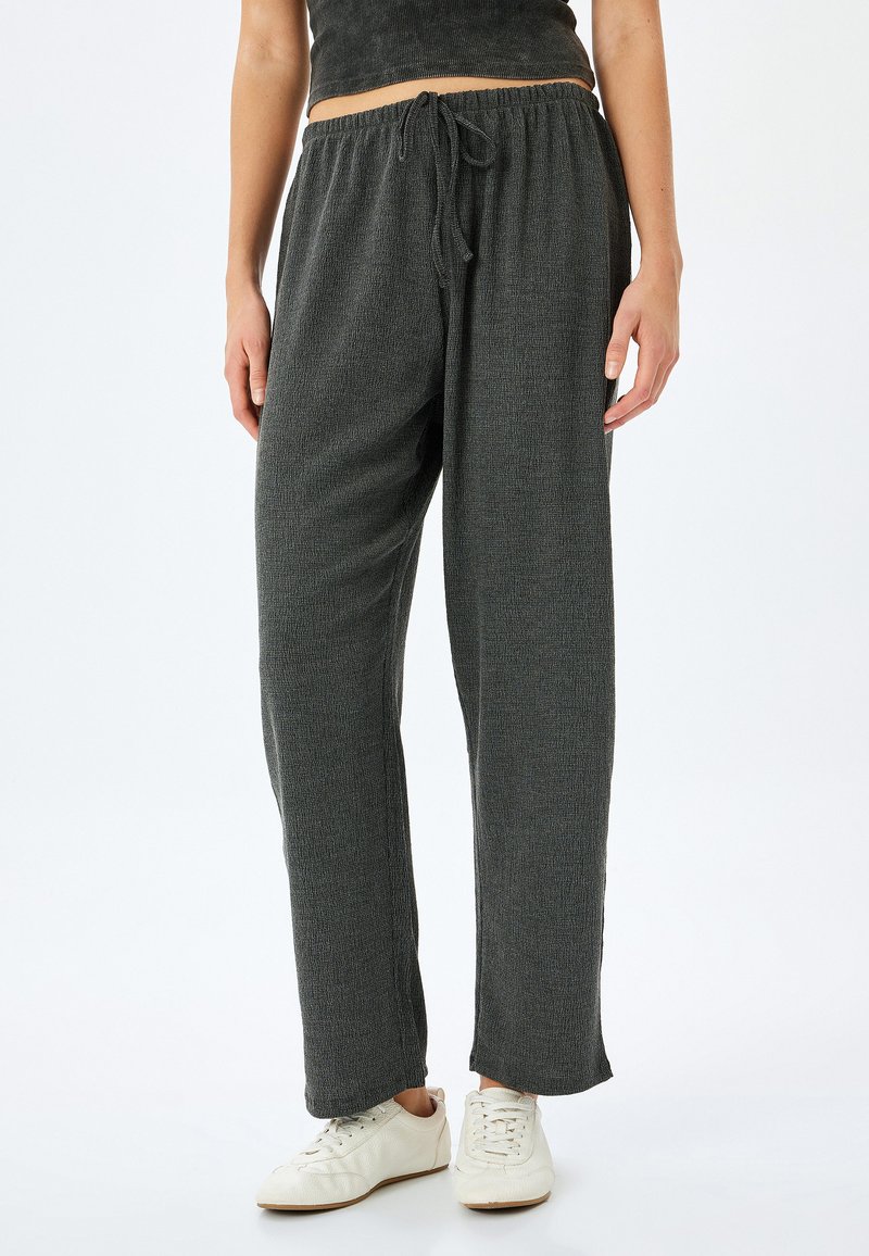 Los pantalones grises, texturizados y de corte holgado cuentan con una cintura elástica con cordón. El modelo los combina con calzado ligero y casual.