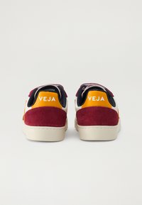 Veja tennised, millel on segu burgundi sametist, valgest nahast ja erksatest oranžidest detailidest, beež kummist tald ja logo kandadel.