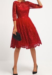 Röd spetsklänning med trekvartslånga ärmar, figursydd överdel och vid kjol. Kombinerad med en svart kuvertväska och svarta klackskor.