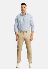 Camisa de botones a rayas en azul y blanco con mangas largas, combinada con pantalones caqui y zapatillas blancas. La camisa presenta un cuello estándar.