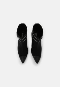 Botines de punto negros hasta el tobillo con punteras afiladas, cuello elástico y detalles de marca en blanco en la base. Textura suave con un diseño ajustado.