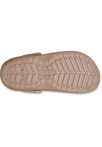 Jasnobrązowa podeszwa Crocs z teksturowym bieżnikiem, z rowkami i wypukłymi wzorami. Wytłoczone logo "CROCS" w pobliżu środka. Zaokrąglony kształt.