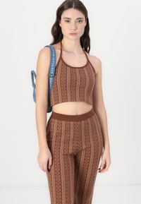 Barna mintás crop top, hozzáillő magas derekú leggings-szel, geometrikus mintázattal és texturált anyaggal. Kék válltáska a vállon.
