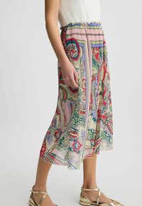 Jupe midi à motifs floraux en tissu léger avec une taille smockée et un design plissé. Les couleurs dominantes incluent le rouge, le vert et la crème.