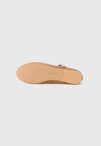 Pohja vaaleanruskeasta mokkasisäisestä nilkkasaappaasta, jossa on litteä kumipohja ja "Steve Madden" -logo painettuna pohjaan.