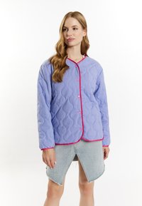 Lyse lilla quiltet jakke med pink accentpiping og knapper. Har lange ærmer og en rundet fald. Bæres over en denimnederdel.