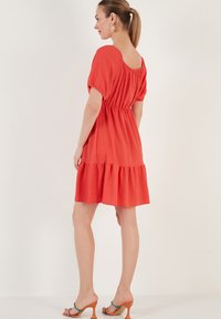 Red tiered dress with short puff sleeves, gathered waist, and a textured fabric. Features a scoop back and falls above the knee.